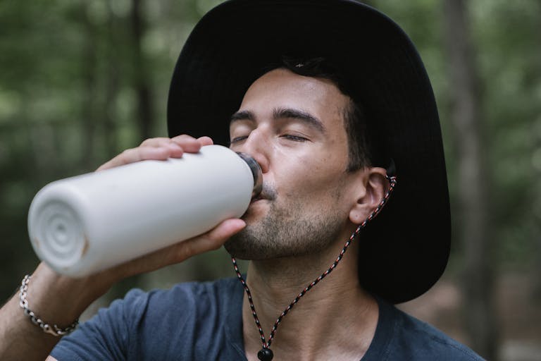 Close-up of a man drinking from a water bottle in a forest setting, capturing a refreshing moment outdoors.