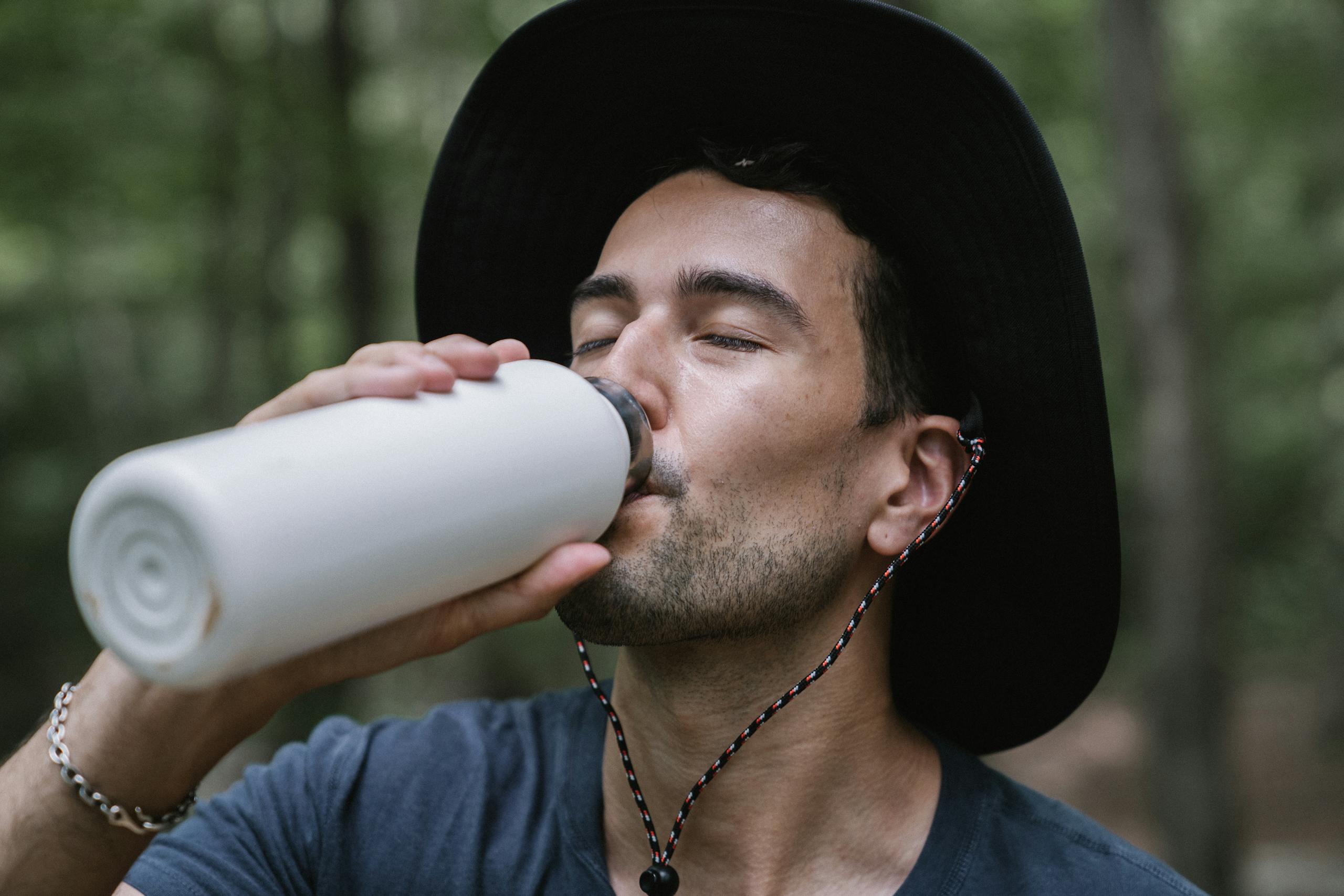 Close-up of a man drinking from a water bottle in a forest setting, capturing a refreshing moment outdoors.