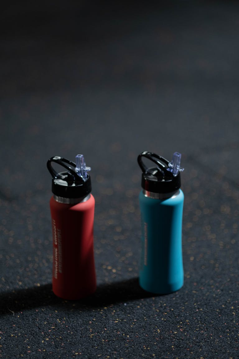 Two vibrant sports bottles on a dark textured floor, blue and red.