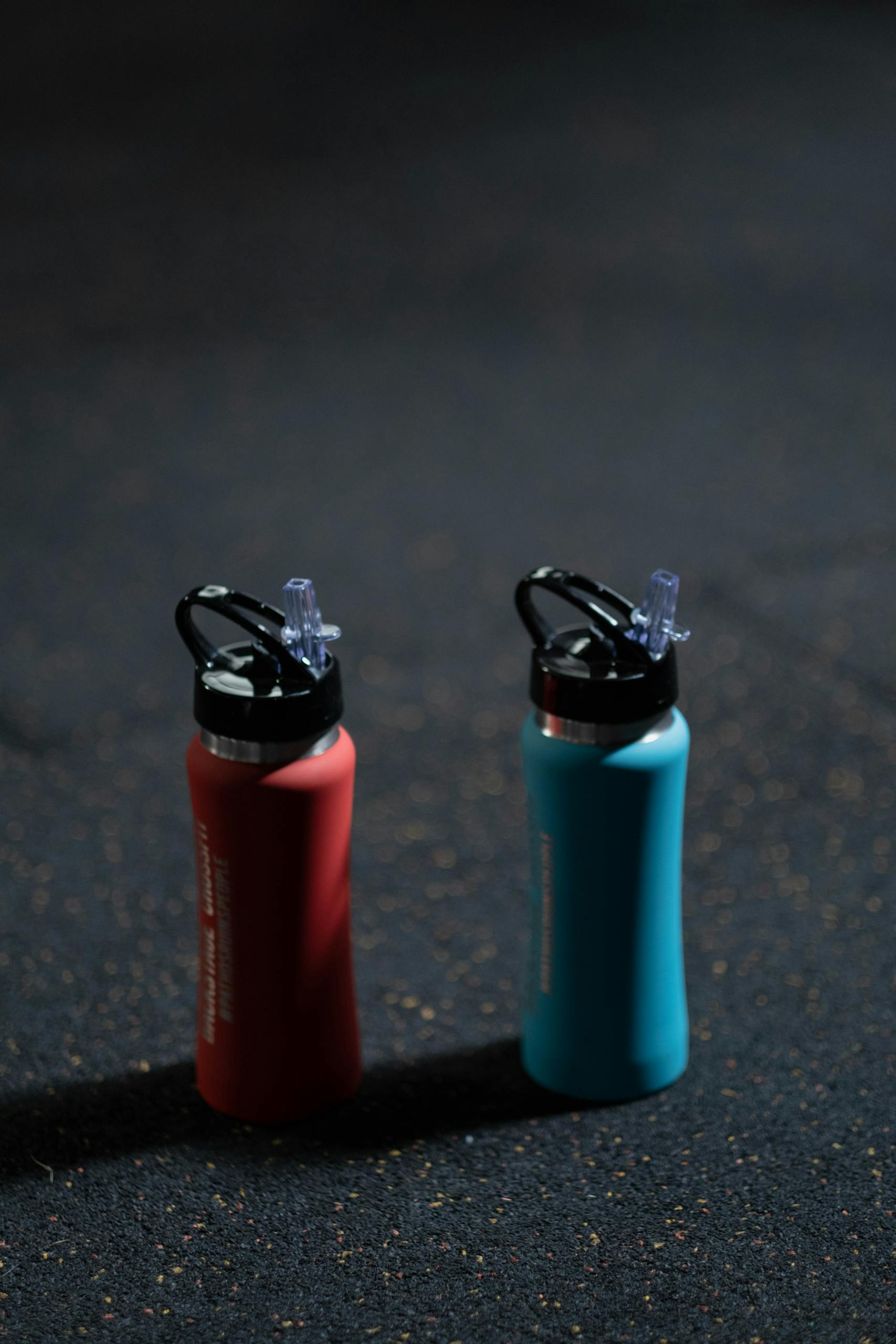 Two vibrant sports bottles on a dark textured floor, blue and red.